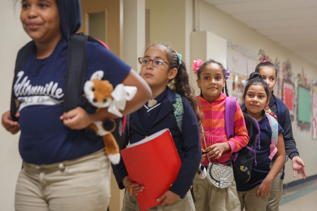 A group of elementary students eagerly line up in the hallway of their school awaiting recess.