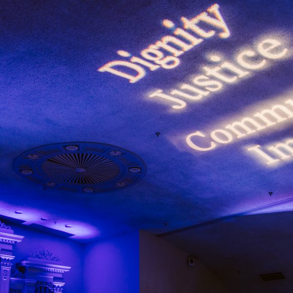 The words “dignity,” “justice,” “community,” and “impact,” are projected onto a high ceiling.