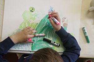 young boy with markers draws picture of landscape and monsters.