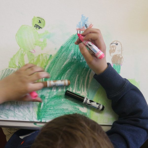 young boy with markers draws picture of landscape and monsters.